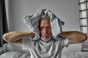 An Old Man Holding A Pillow Over His Head